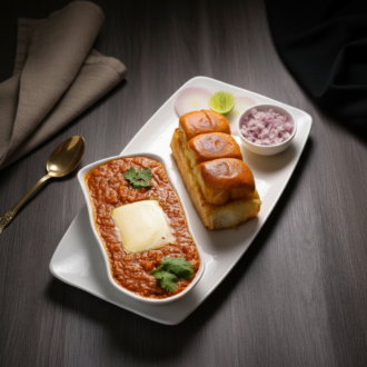 A classic Mumbai-style Pav Bhaji platter featuring a rich vegetable gravy topped with a melting slab of butter, served with three toasted pav buns, chopped onions, and lemon.